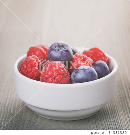 raspberries and blueberries in white bowl 34381389