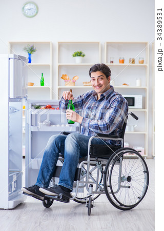 Young disabled injured man opening the fridge door Young disabled injured man opening the fridge door 34389531