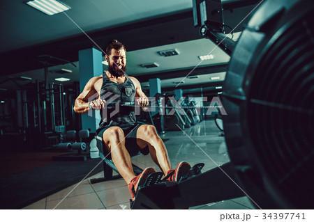 Muscular fit man using rowing machine at gym 34397741