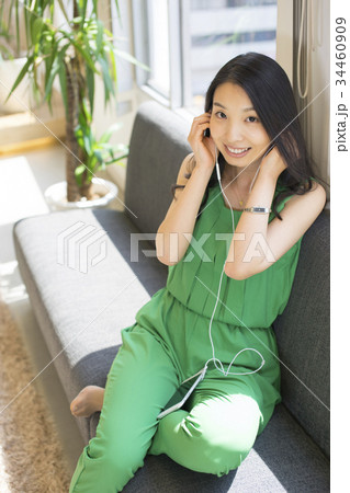 日差しが心地良い窓際のソファに横になりスマートフォンでダウンロードした音楽を楽しむロングヘアーの女性 34460909