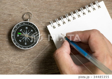 Man hold pen to write on note book with compass 34485355