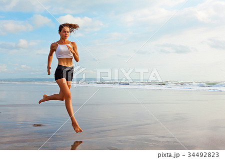 Sporty girl running by beach along sea surf 34492823