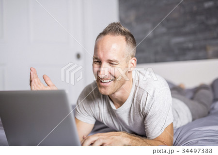 Serious casual young man using laptop in bed at 34497388