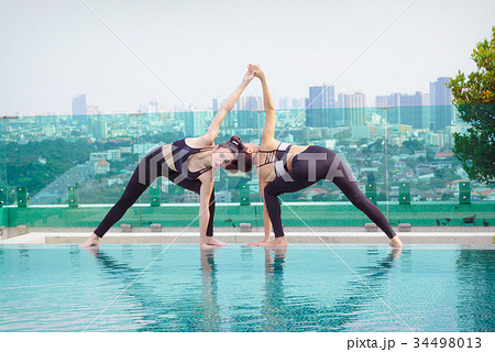 Two women doing yoga pose at the swimming pool Two women doing yoga pose at the swimming pool 34498013