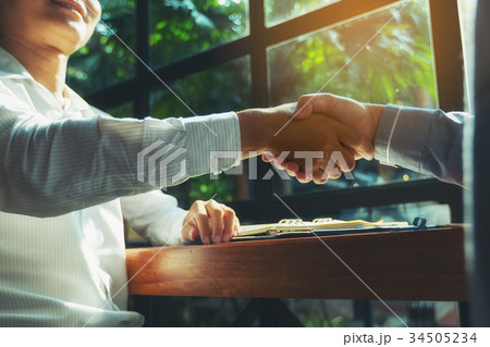 Two businessmen sit and shake hands at the coffee shop window af 34505234