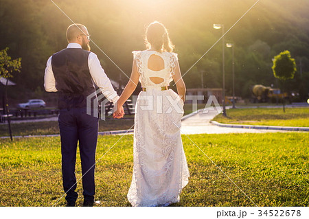 Bride and groom walking towards sunset holding hands Bride and groom walking towards sunset holding hands 34522678