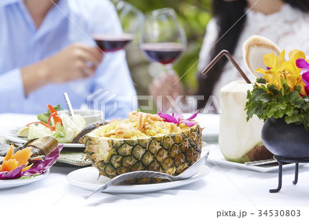 A couple is clinking wine glasses with several of Thai foods on the table. 34530803
