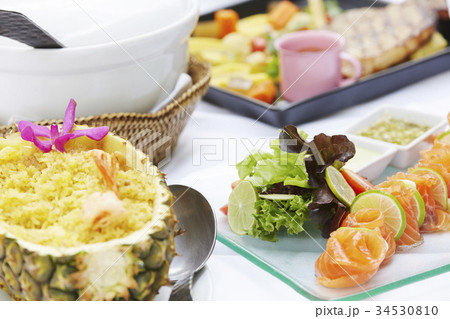 Image of several dishes of food including fried rice in pineapple, spicy salmon salad and steak on a white table. 34530810