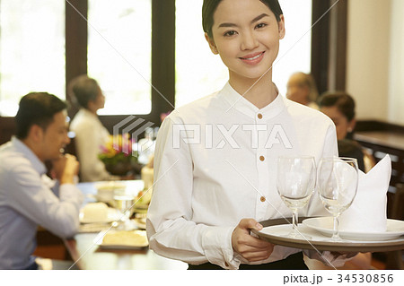 the happy waitress is bringing a tray with glasses and napkin. the happy waitress is bringing a tray with glasses and napkin. 34530856