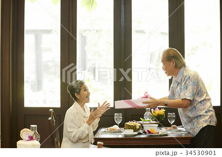 Asian senior man giving his surprised wife a gift at restaurant Asian senior man giving his surprised wife a gift at restaurant 34530901