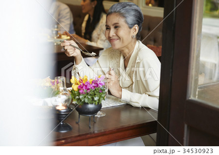 An older woman is having lunch near the window in a restaurant An older woman is having lunch near the window in a restaurant 34530923