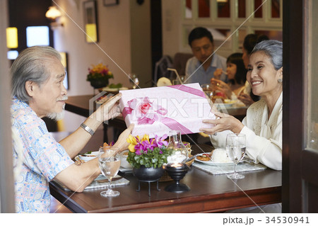 a senior couple is holding gift box, smiling and looking at each other. a senior couple is holding gift box, smiling and looking at each other. 34530941