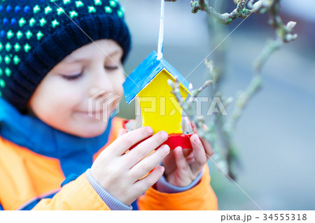 Little kid hanging bird house on tree for feeding Little kid hanging bird house on tree for feeding 34555318
