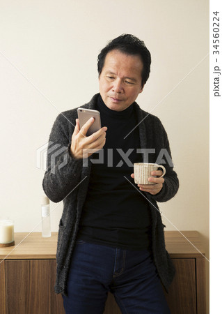 カップを持ちスマホを操作する60代男性 34560224