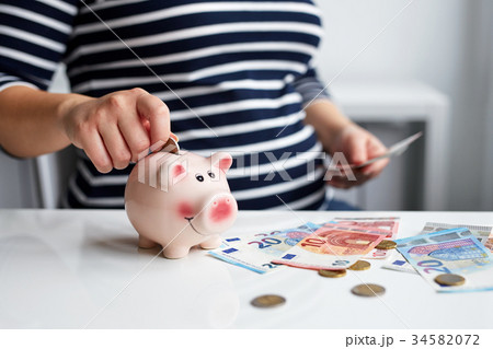 Pregnant woman putting coin into piggy bank 34582072