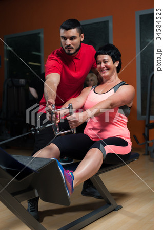 Young male coach assisting female client in gym 34584525