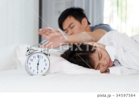Sleepy man trying turn off alarm clock 34597564