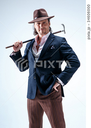 The mature man in a suit and hat holding cane. 34606000