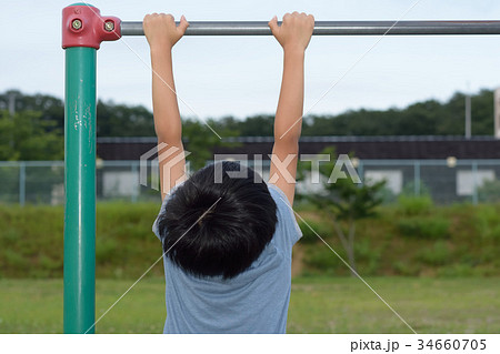 鉄棒にぶら下がる男の子の写真素材