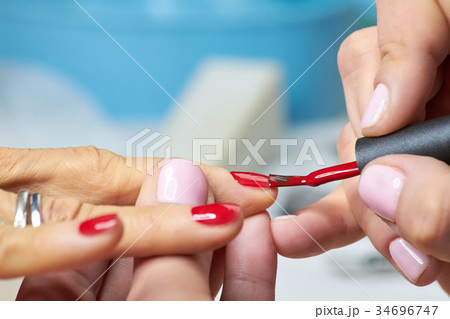 Beautician applying red varnish to finger nails. 34696747