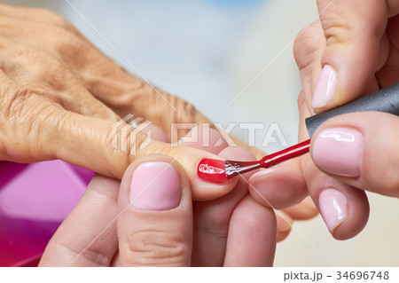Manicurist applying red varnish to senior woman. 34696748