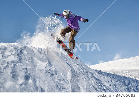 Stylish snowboarder with helmet and mask jumps 34705083