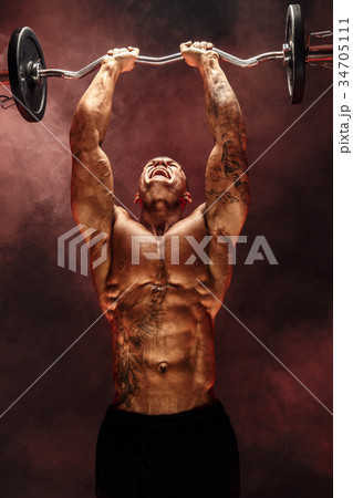 Strong sportsman lifting heavy dumbbell in smoke Strong sportsman lifting heavy dumbbell in smoke 34705111