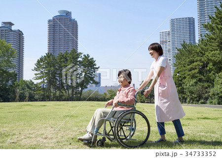 車いすで散歩する笑顔のシニアとヘルパーさん 34733352