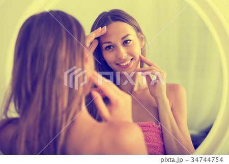 woman examining her face by looking at it in mirror 34744754