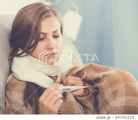 Sick girl on sofa with thermometer 34745225