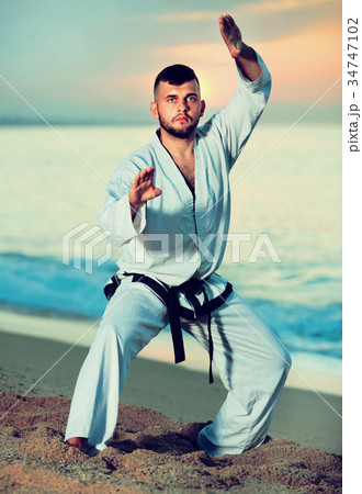 Man in uniform doing taekwondo exercises at sunset sea shore Man in uniform doing taekwondo exercises at sunset sea shore 34747102