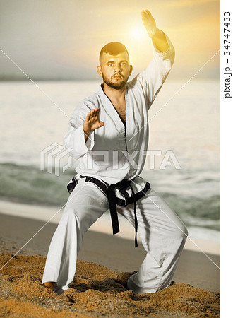 Man in uniform doing taekwondo exercises at sunset sea shore 34747433