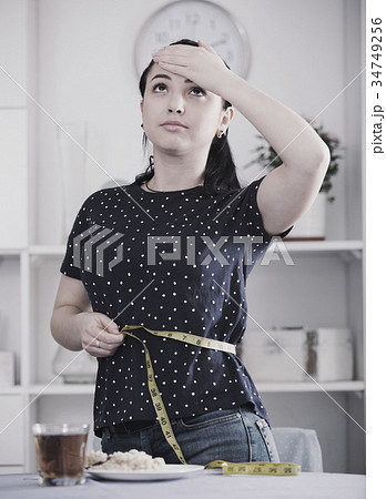 Frustrated girl measuring waistline Frustrated girl measuring waistline 34749256