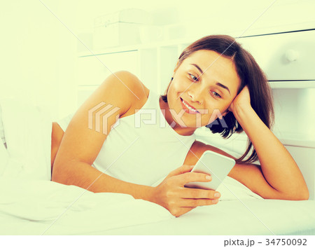 Woman using phone in bed Woman using phone in bed 34750092