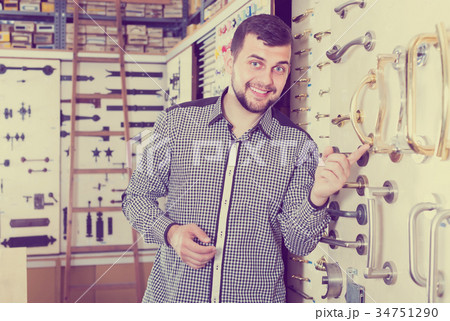 satisfied male customer examining various door handles in store 34751290