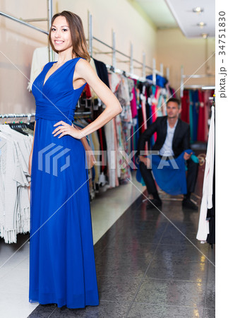 Young cheerful female is trying on new dark blue dress Young cheerful female is trying on new dark blue dress 34751830