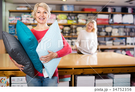 Smiling senior seller is showing wide assortment of pillows Smiling senior seller is showing wide assortment of pillows 34752356