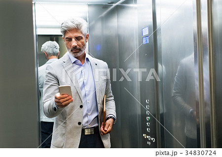 Mature businessman with smartphone in the elevator 34830724