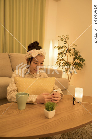 夜、部屋着でスマホを見ながら寛ぐ女性 34840610
