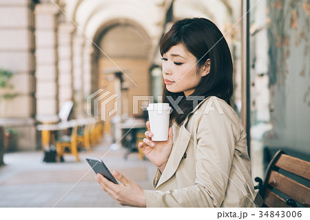 ベンチでコーヒーを飲みながらスマホを見る女性 ベンチでコーヒーを飲みながらスマホを見る女性 34843006