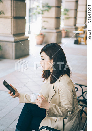 ベンチでコーヒーを飲みながらスマホを見る女性 ベンチでコーヒーを飲みながらスマホを見る女性 34843025