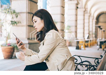 ベンチでコーヒーを飲みながらスマホを見る女性 ベンチでコーヒーを飲みながらスマホを見る女性 34843029