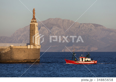 Spain, Andalusia, Tarifa, port of Tarifa, Jesus Christ statue by sea and red fishing boat 34865658