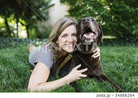 Portrait of smiling woman lying on grass with Labrador Retriever Portrait of smiling woman lying on grass with Labrador Retriever 34866264