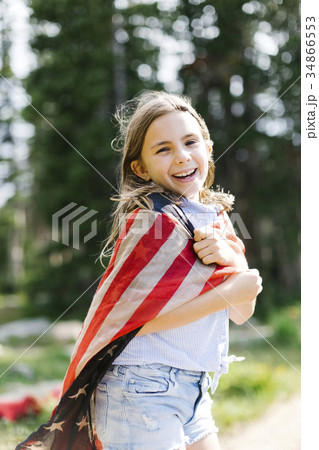 Portrait of girl (8-9) wrapped in us flag in forest 34866553