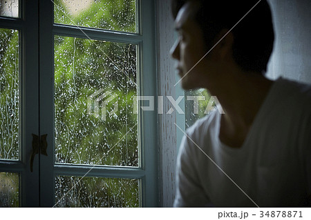 雨の日 窓の外を眺める男性の写真素材