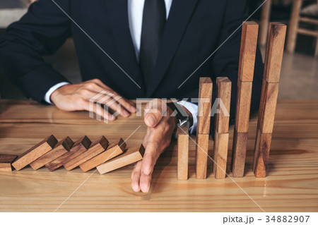 Close up of businessman hand Stopping Falling wooden Dominoes ef Close up of businessman hand Stopping Falling wooden Dominoes ef 34882907