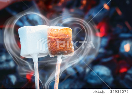 Two white sweet marshmallows roasting over fire 34935073