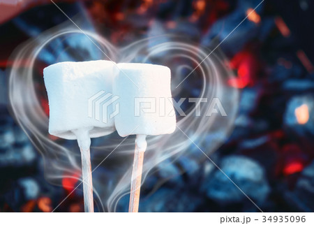 Two white sweet marshmallows roasting over fire 34935096