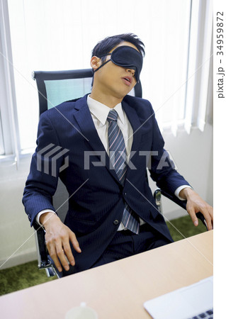 アイマスクを付け会社事務所で仮眠休憩するスーツ姿の若い営業ビジネスマン 34959872